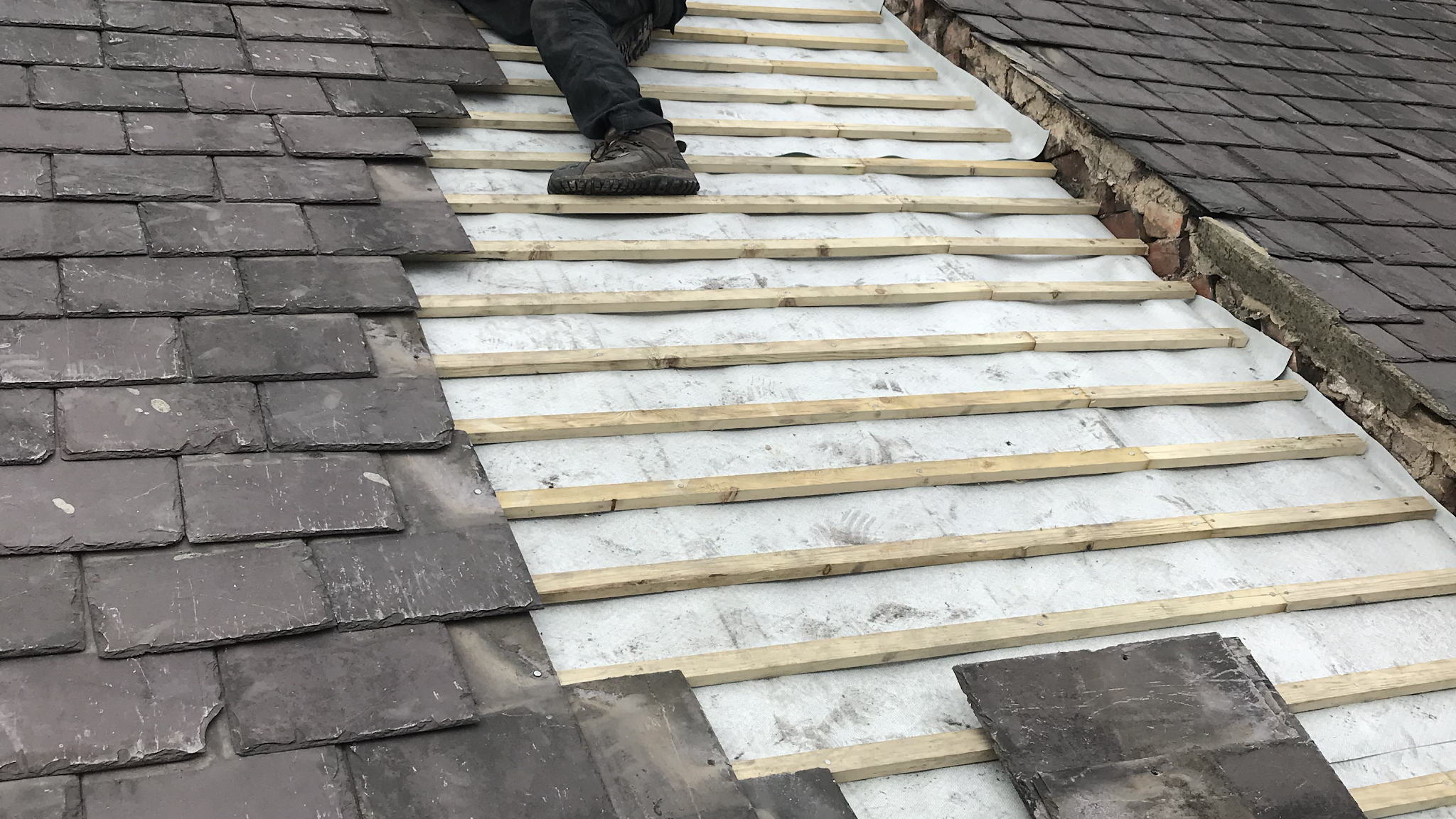 New pale timber battens laid in rows over white membrane between two sections of slate roof