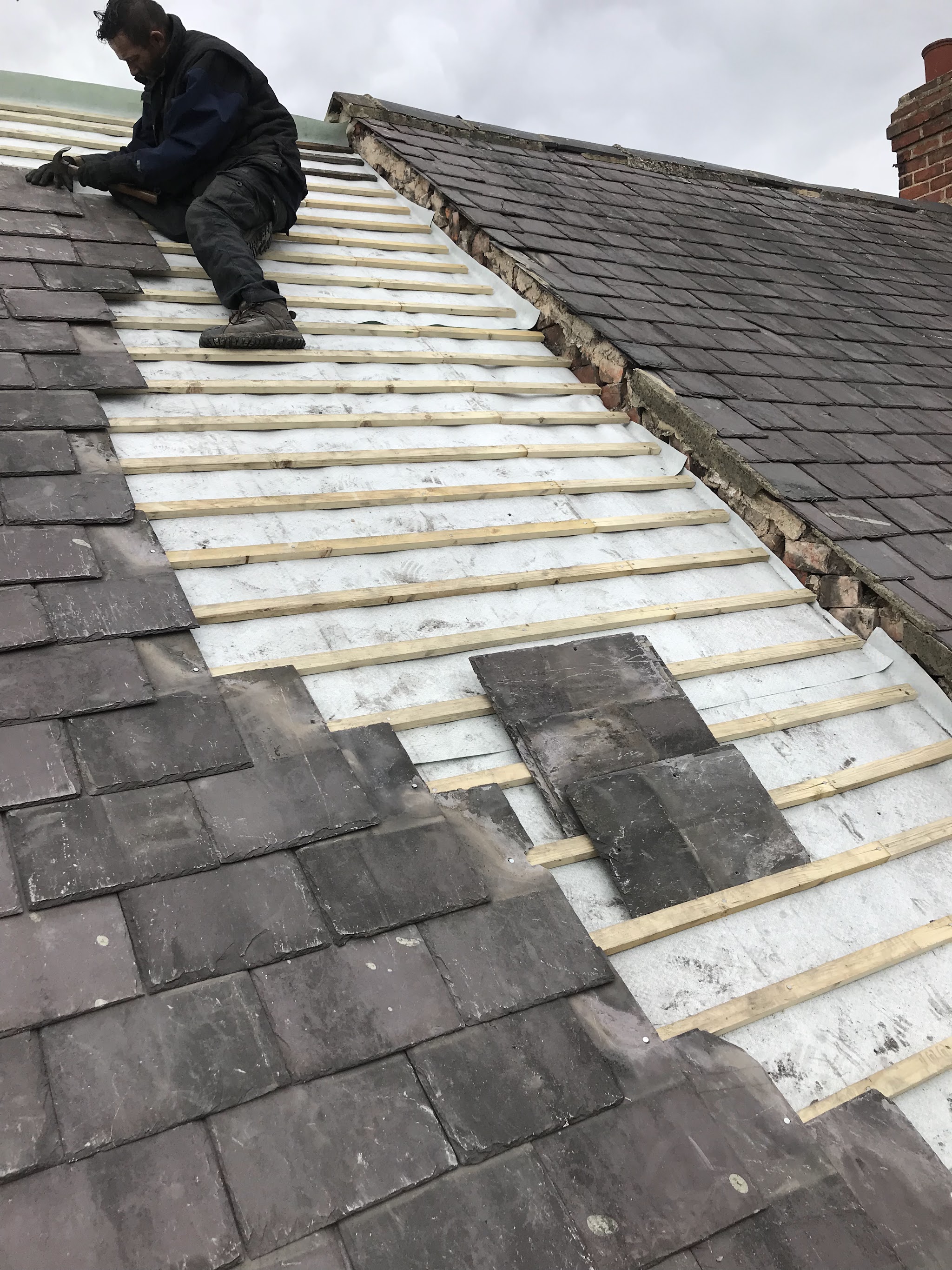 A C&M roofer sitting on new battens, laying slates back on a roof