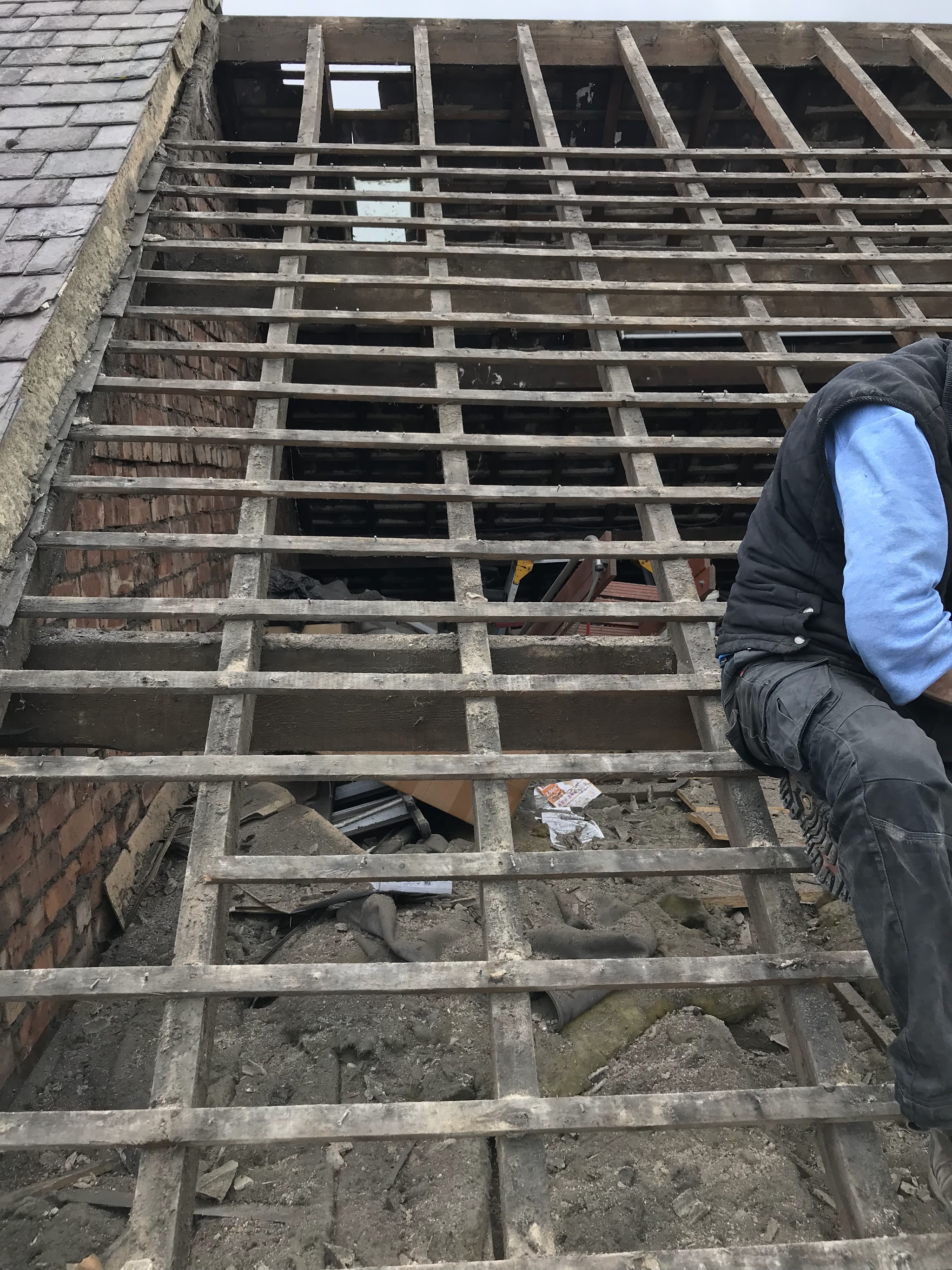 A slate roof stripped down to the rafters and old battens, with one of the C&M team sitting on the roof