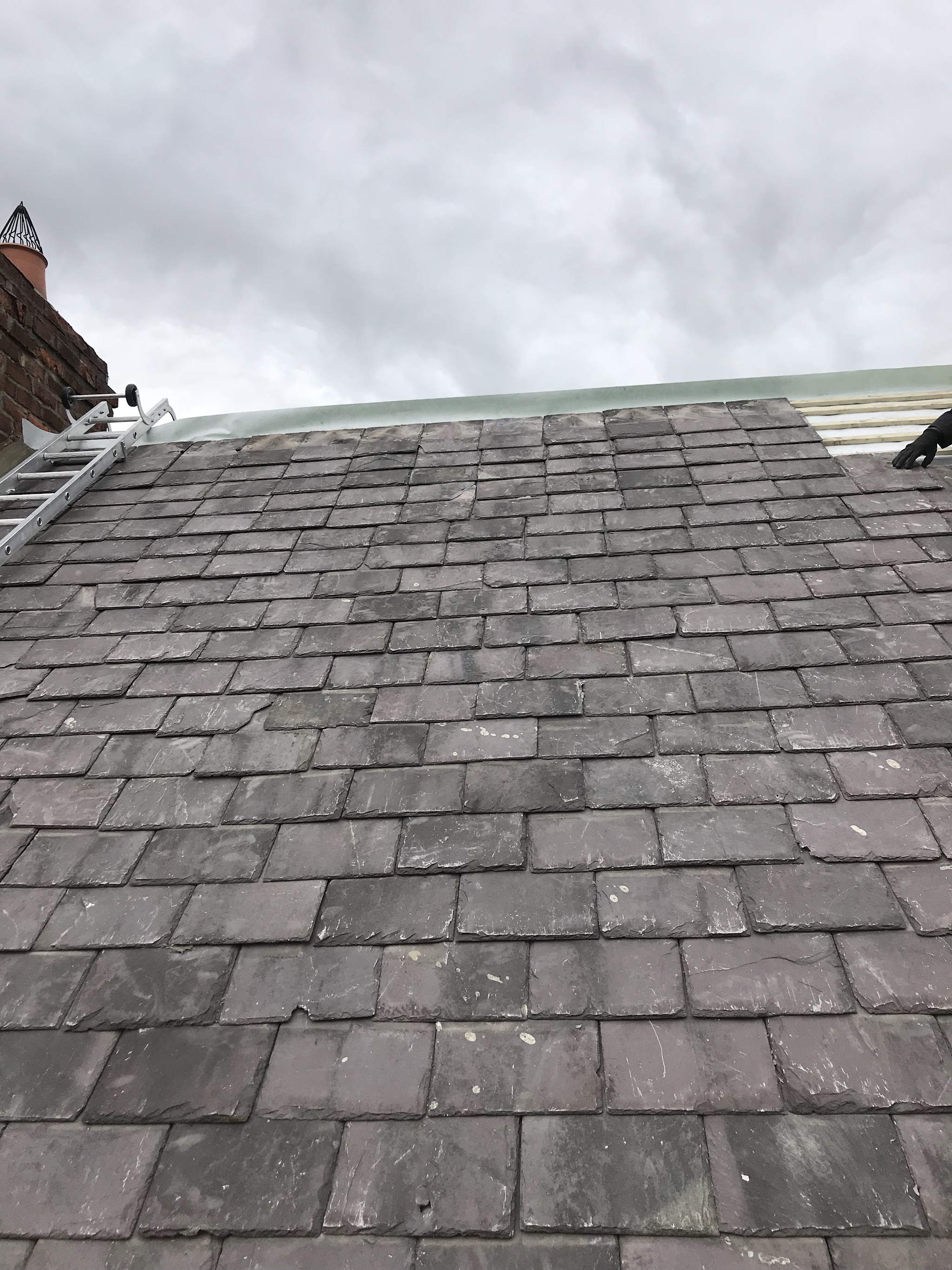 A finished slate roof slope with a new ridge, under a cloudy sky