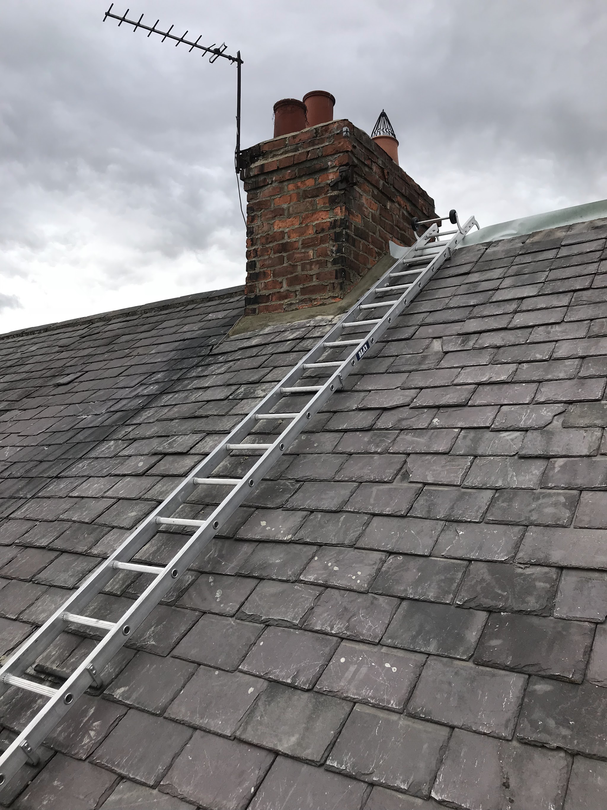 A finished slate roof with a roof ladder running up beside a brick chimney stack